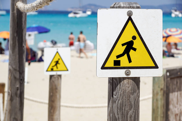 Sinal de aviso de queda, caindo do sinal de aviso de triângulo amarelo na praia
 - Foto, Imagem