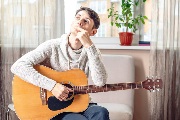 Giovane musicista maschio attraente seduto su una sedia con una chitarra acustica. Il concetto di musica come hobby
 - Foto, immagini