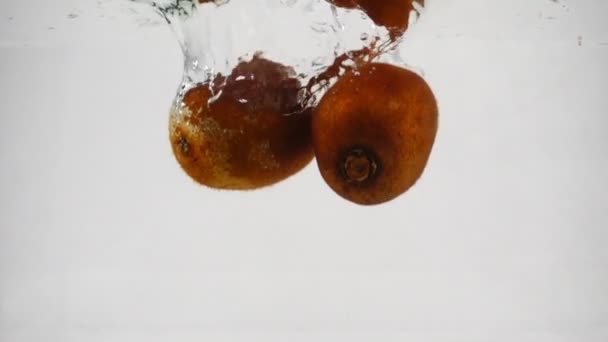 El kiwi en la piel cae al agua con un montón de pequeñas burbujas. Frutos sobre fondo blanco aislado
. - Metraje, vídeo