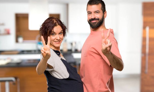 Paar mit schwangerer Frau lächelt und zeigt Siegeszeichen im Haus - Foto, Bild