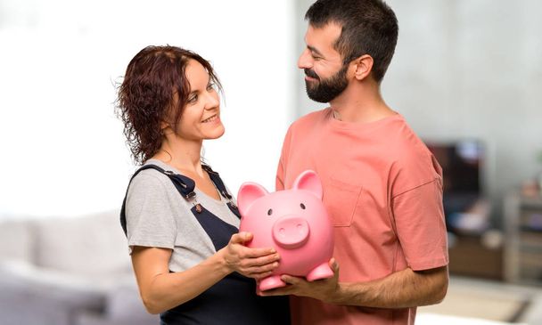 Couple with pregnant woman holding a piggybank inside house - Fotoğraf, Görsel