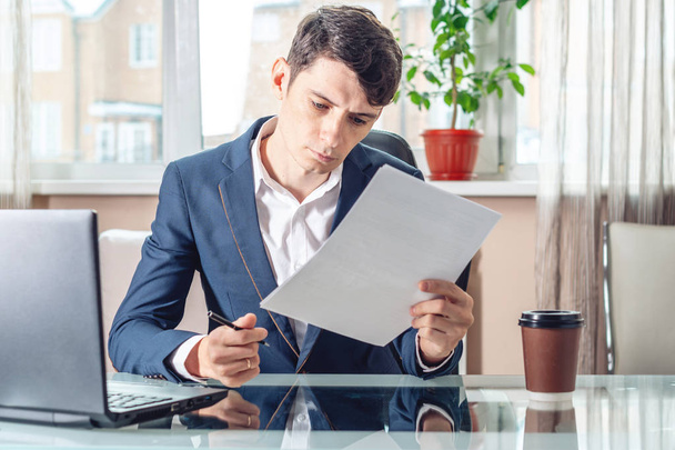 Мужчина-бизнесмен, сидящий на рабочем месте, изучает документы. Концепция работы офиса с документами
 - Фото, изображение