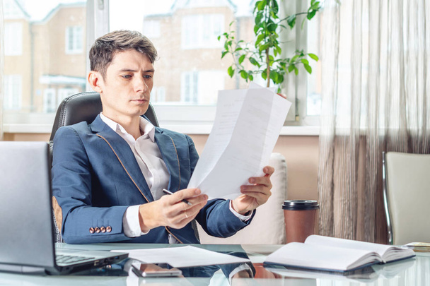 männlicher Manager, der an einem Arbeitsplatz sitzt und Dokumente prüft. das Konzept des Büros, das mit Dokumenten arbeitet - Foto, Bild