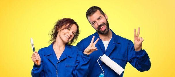 Painters smiling and showing victory sign with both hands on colorful background - Фото, изображение