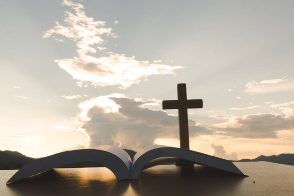 Open Bijbel, script in vervagen met focus op palm cross, op sunrise achtergrond, kruisbeeld, symbool van het geloof. - Foto, afbeelding