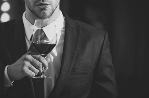 wine glass in hand of man or businessman with beard and hairstyle in formal outfit with red tie near mirror, meeting and relax, bar and restaurant, sommelier, tasting and degustation - Foto, Bild