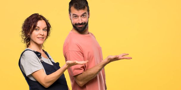 Echtpaar met zwangere vrouw een idee presenteren terwijl op zoek naar glimlachend op gele achtergrond geïsoleerd - Foto, afbeelding