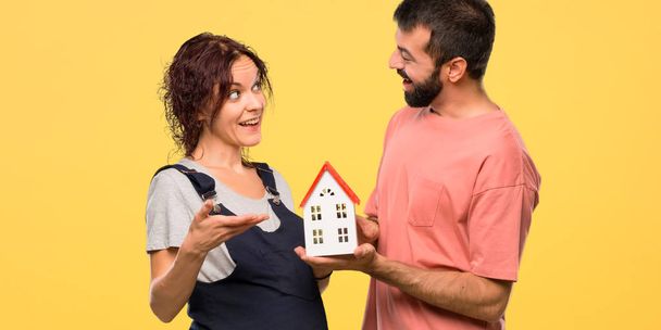 Coppia con donna incinta in possesso di una piccola casa su sfondo giallo isolato
 - Foto, immagini
