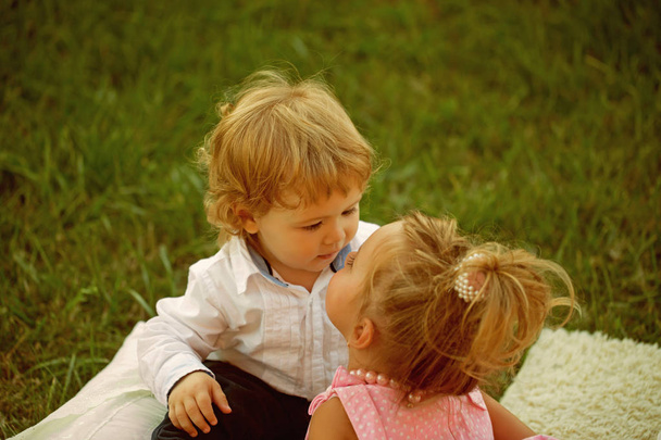 Sister kiss brother with blond hair on green grass - Foto, imagen