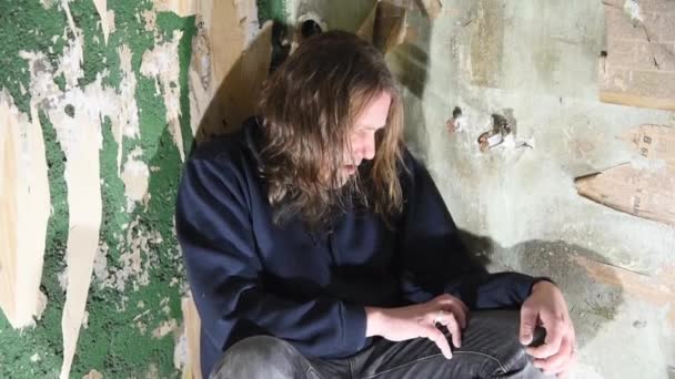Deprimido y enojado hombre está sentado en la esquina en una casa abandonada
 - Imágenes, Vídeo