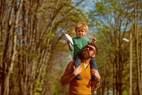 Father give son piggyback launching paper plane toy. Little child play with toy in park. Up, up, and away - Фото, зображення