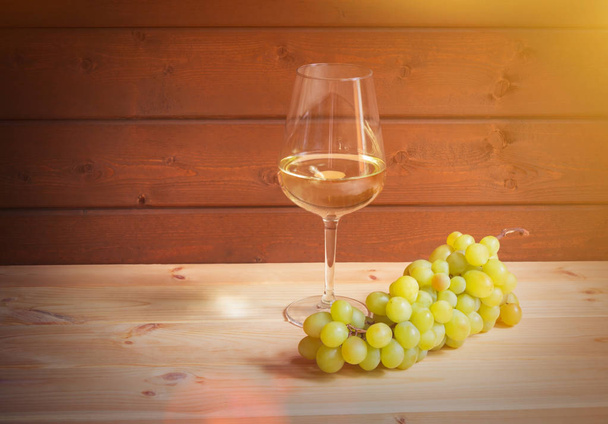 Glass of white wine and green grape branch on wooden table. View with copy space. - Фото, изображение