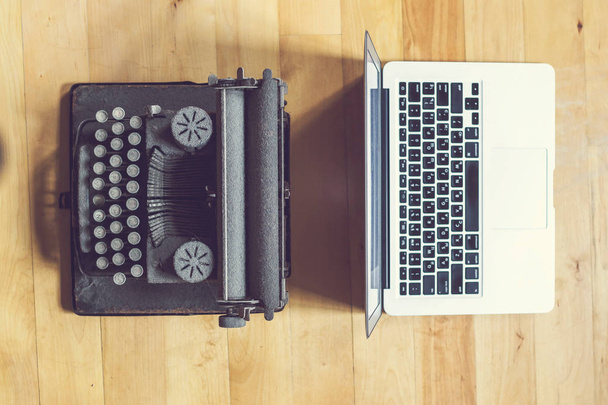 old vintage dust-covered typewriter with sheet of white paper near modern notebook on bookcase background. modern technology and vintage appliances - 写真・画像