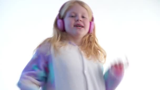 moderne Mode - schönes blondes Mädchen hört Musik mit Kopfhörern und tanzt auf weißem Hintergrund im kigurumi-Pyjama - isoliert auf weiß - Filmmaterial, Video