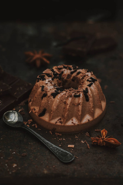 Italiaans dessert. Panna cotta op donkere chocolade, met een chocolade kruik en hagelslag op een donkere achtergrond - Foto, afbeelding
