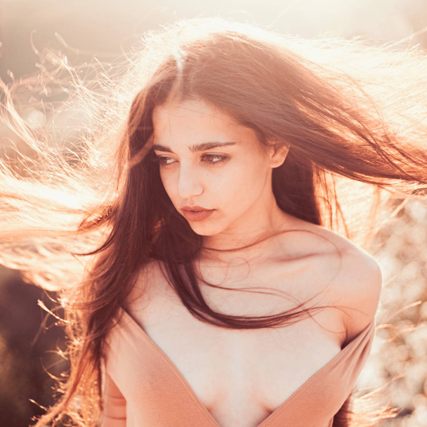 Girl with decollete enjoy her hair waving by wind. Woman on calm face enjoy sunny and windy day, nature on background, defocused. Lady looks attractive with waving long hair. Hair care concept. - 写真・画像
