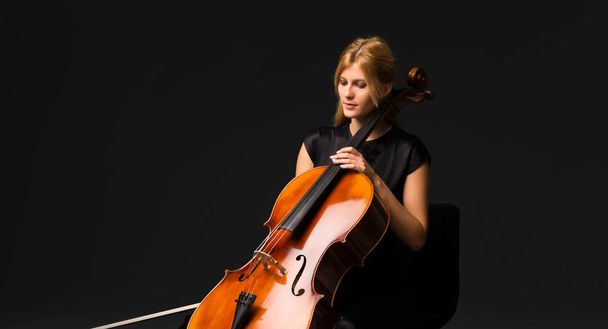 Young girl playing the cello on isolated black background - Foto, Bild