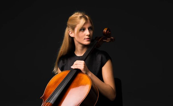 Young girl playing the cello on isolated black background - Photo, Image