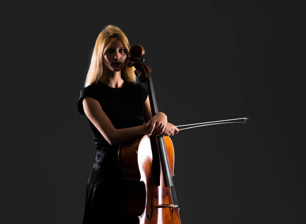 Young girl playing the cello on isolated black background - Photo, Image