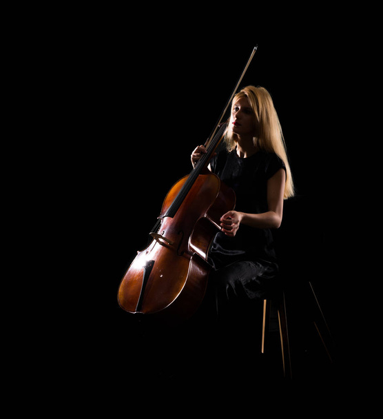 Young girl playing the cello on isolated black background - Foto, imagen