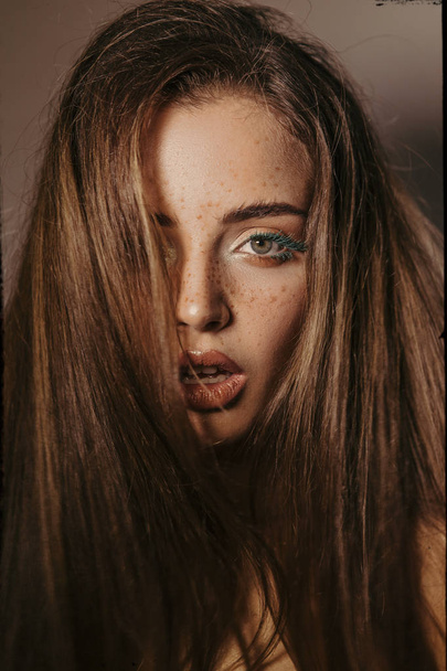 Portret van de schoonheid van een mooi meisje met make-up, volumineuze kapsel en oorbellen, kijken naar de camera - Foto, afbeelding