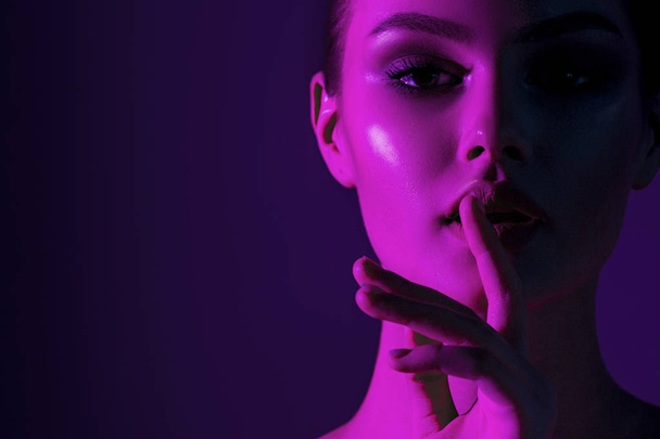Tsss... Young beautiful girl with magenta neon lighting. Emotional beauty close-up portrait - Фото, изображение