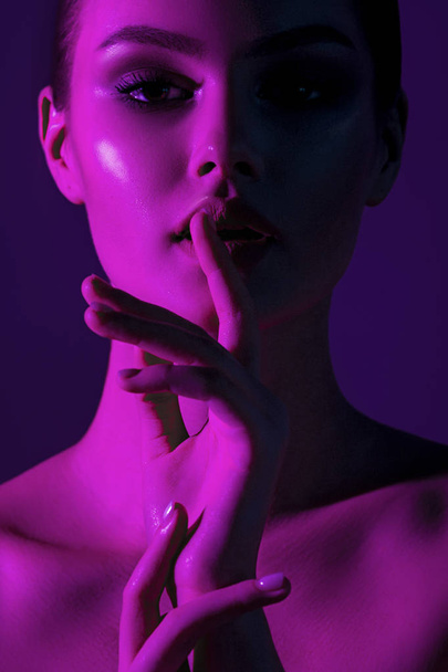 Tsss... Young beautiful girl with magenta neon lighting. Emotional beauty close-up portrait - Foto, Imagem