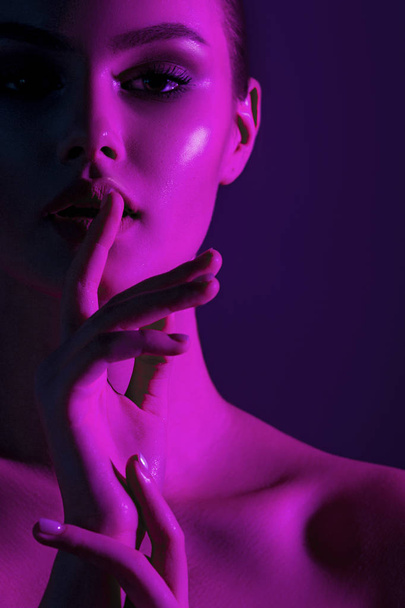 Tsss... Young beautiful girl with magenta neon lighting. Emotional beauty close-up portrait - Zdjęcie, obraz