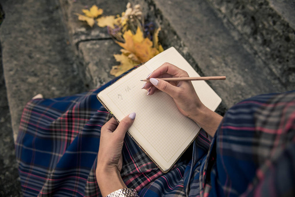 κορίτσι με τα μπλε σε ένα καμαρίνι καθισμένος στα σκαλιά και γράφοντας ένα μολύβι σε ένα σημειωματάριο - Φωτογραφία, εικόνα