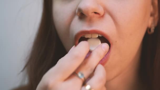 Close up image of woman putting white round pill in mouth. Sick female taking medicines, antidepressant, painkiller or antibiotic. Young lady drinking contraceptives. Pharmacy and healthcare concept - Materiał filmowy, wideo