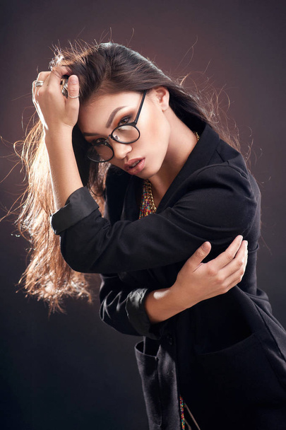Portrait of a beautiful girl in round glasses on a brown background in the studio, the concept of beauty - 写真・画像