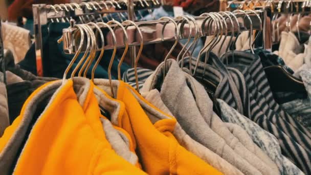 Μεγάλο αριθμό πολύχρωμα ζεστό χειμώνα πουλόβερ κολλάει στις κρεμάστρες στο κατάστημα του εμπορικό κέντρο, αγοραστές περνούν. - Πλάνα, βίντεο