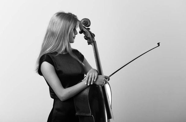 junges blondes Mädchen mit ihrem Cello posiert auf weißer Wand - Foto, Bild