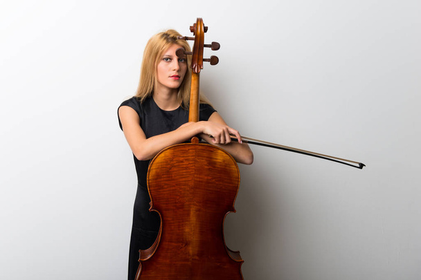 Young blonde girl with her cello posing on white wall - Foto, Imagen