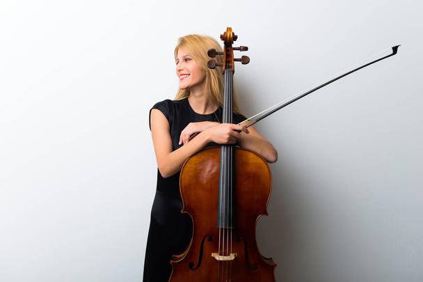 Giovane ragazza bionda con il suo violoncello posa su parete bianca
 - Foto, immagini