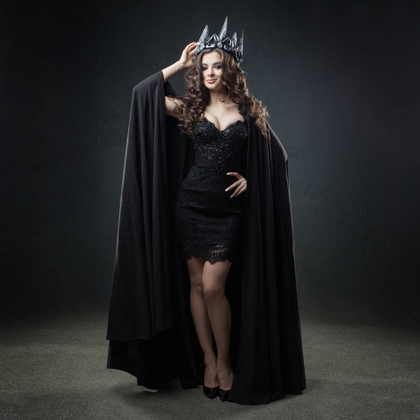 The dark Queen. Attractive and sexy young woman in long black cloak and crown. - Fotoğraf, Görsel