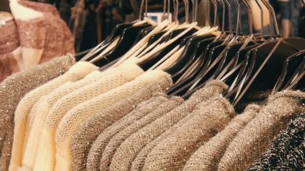 Fila de hermosas mujeres cálidas suéteres esponjosos de gris, negro y blanco están colgando de perchas negras en la tienda del centro comercial o centro comercial. Colección a la moda de la ropa de abrigo
. - Metraje, vídeo