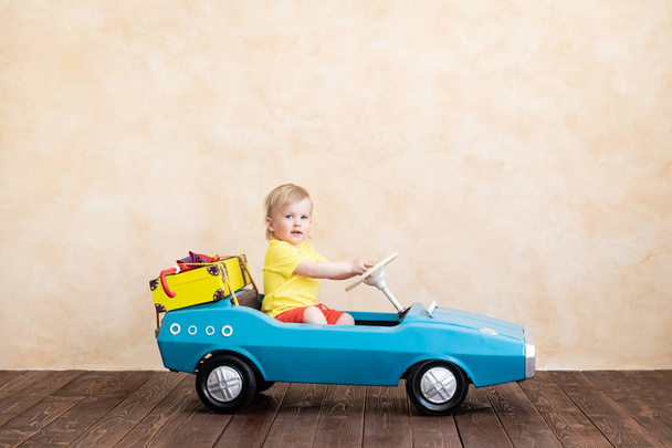 Happy child toddler riding toy vintage car model with suitcase at home.  - Foto, afbeelding