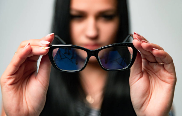 Portrait of woman on blurred background holding focused protective optical eyeglasses isolated in studio. Test examination health care concept - Valokuva, kuva