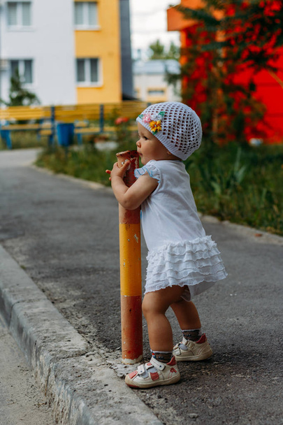 Schattig meisje plezier op zomerdag. een klein meisje staat op het pad van de overgang en de vastklampt aan het hek, pijp - Foto, afbeelding