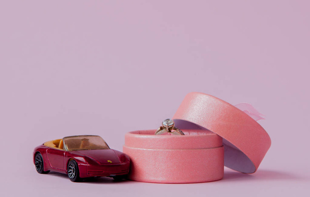 Spielzeugauto mit Ehering-Box auf rosa Hintergrund mit Kopierraum - Foto, Bild