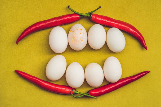 Eggs and red pepper in the form of a mouth with teeth. One of the teeth is sick in the form of a cracked egg. Sick tooth concept - Foto, Bild
