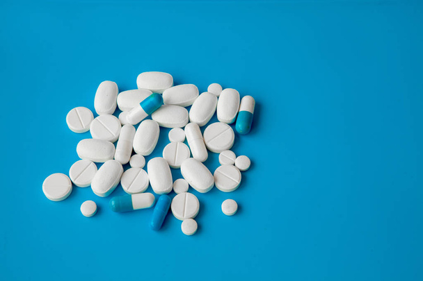 Scattered white pills on blue table. Mock up for special offers as advertising, web background or other ideas. Medical, pharmacy and healthcare concept. Copy space. Empty place for text or logo. - Photo, image