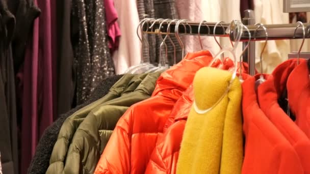 Διάφορα πολύχρωμα ζεστά Γυναικεία ρούχα που κρέμονται στις κρεμάστρες σε ένα κατάστημα ενδυμάτων στη λεωφόρο ή το εμπορικό κέντρο - Πλάνα, βίντεο