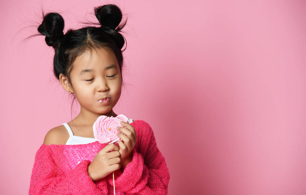 幸せな若いアジア小さな女の子子供舐める食べる幸せの大きな甘いロリーポップ キャンディー ピンク  - 写真・画像