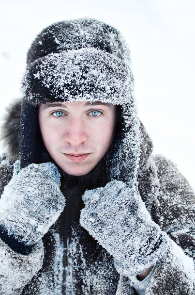 portrait of a young guy in a snow-covered coat and hat - Photo, Image