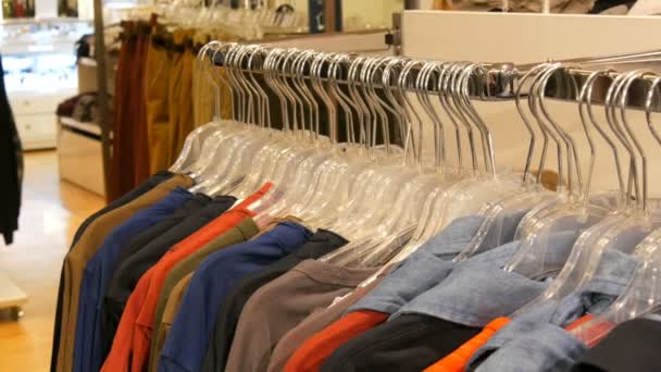 Διάφορα πολύχρωμα ρούχα που κρέμονται στις κρεμάστρες σε ένα κατάστημα ενδυμάτων στη λεωφόρο ή το εμπορικό κέντρο - Πλάνα, βίντεο