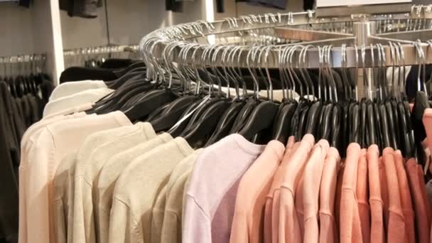 Op een grote ronde hanger zijn er verschillende stijlvolle gebreide veelkleurige truien opknoping op mode zwarte hangers in een kledingwinkel in een winkelcentrum of winkelcentrum, close-up - Video