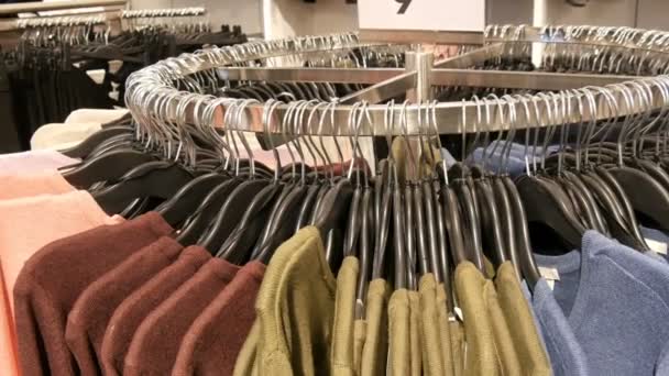 En una gran percha redonda hay varios suéteres multicolores de punto elegantes que cuelgan de perchas negras de moda en una tienda de ropa en un centro comercial o centro comercial, vista de cerca
 - Metraje, vídeo