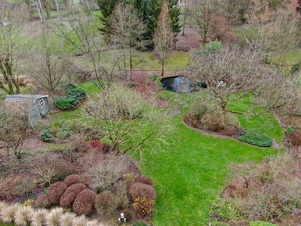 Vue aérienne du beau type de jardin anglais pendant la saison hivernale. Vue panoramique d'un beau jardin de style anglais avec une grande herbe verte, petite livre d'eau et petite maison de jardin en bois
. - Photo, image